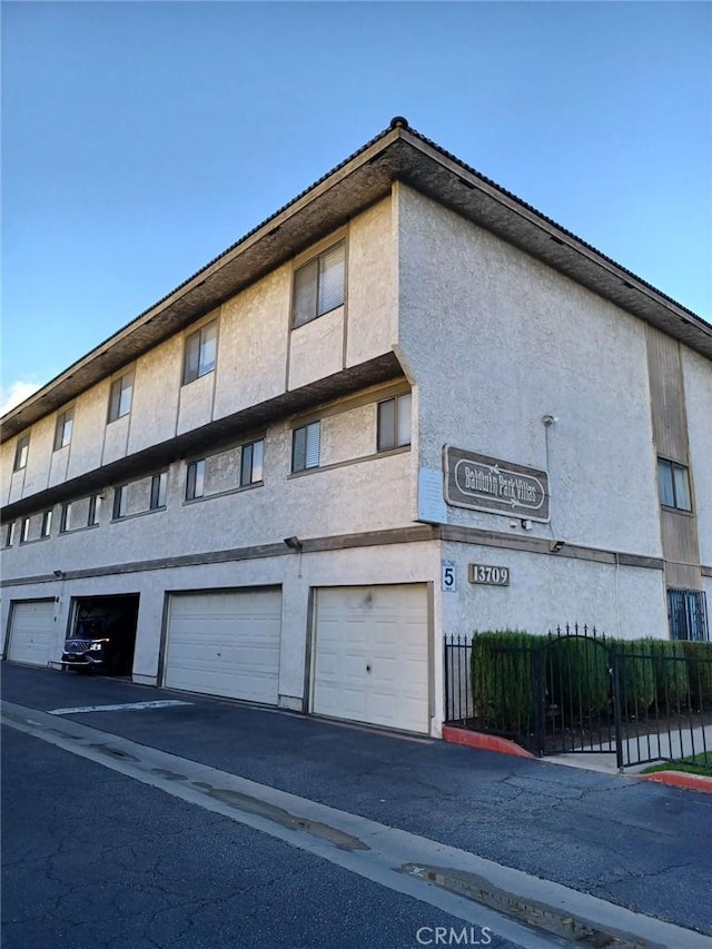 view of building exterior featuring driveway, an attached garage, and fence