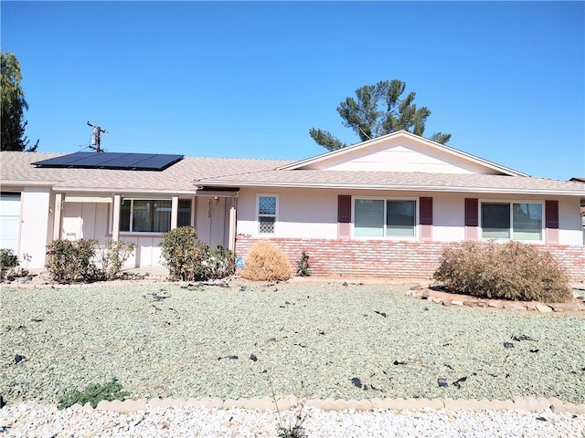 ranch-style house with brick siding, roof mounted solar panels, and stucco siding