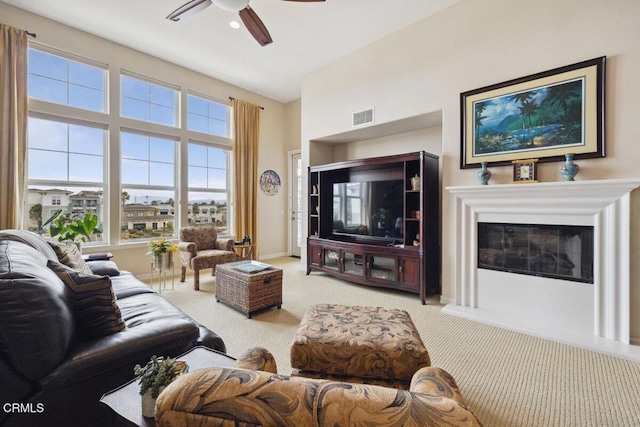 living room with baseboards, visible vents, ceiling fan, a glass covered fireplace, and carpet flooring