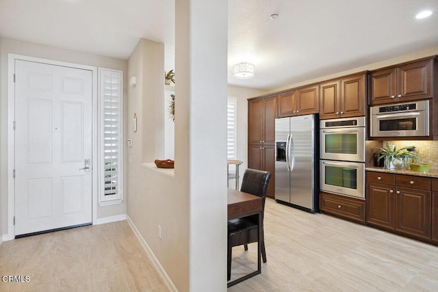 kitchen featuring decorative backsplash, baseboards, appliances with stainless steel finishes, and light stone countertops