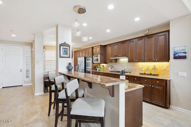 kitchen featuring light stone counters, decorative light fixtures, a kitchen breakfast bar, appliances with stainless steel finishes, and decorative backsplash