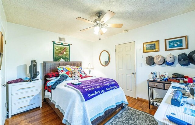 bedroom featuring a ceiling fan, wood finished floors, visible vents, and a textured ceiling