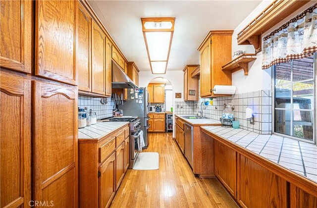 kitchen with tile countertops, ventilation hood, arched walkways, a sink, and stainless steel appliances