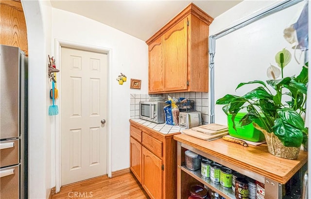 kitchen featuring tile countertops, lofted ceiling, stainless steel appliances, light wood-type flooring, and backsplash