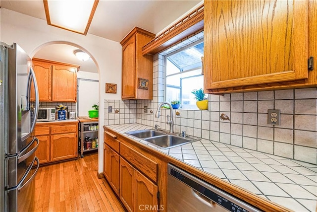 kitchen with brown cabinets, a sink, light wood-style floors, appliances with stainless steel finishes, and tile counters