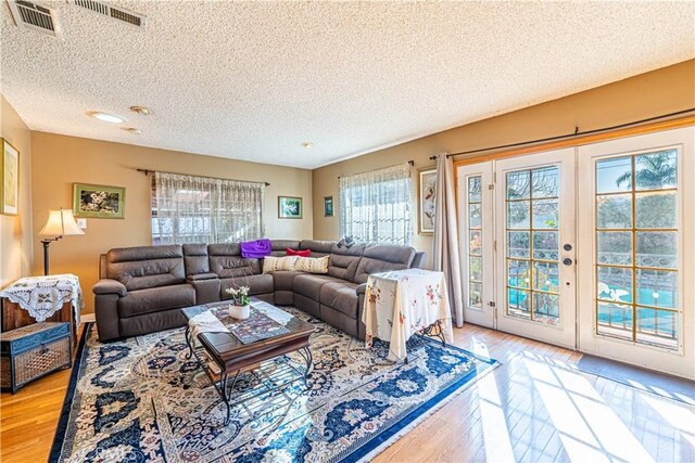 living room with visible vents, french doors, light wood-style floors, and a textured ceiling