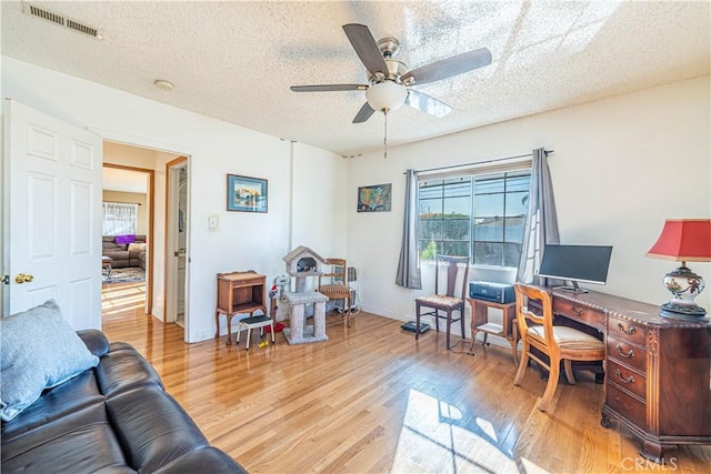 office featuring a ceiling fan, baseboards, visible vents, light wood-style flooring, and a textured ceiling