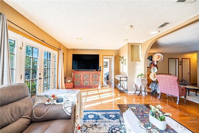 living area with visible vents, a textured ceiling, wood finished floors, french doors, and arched walkways