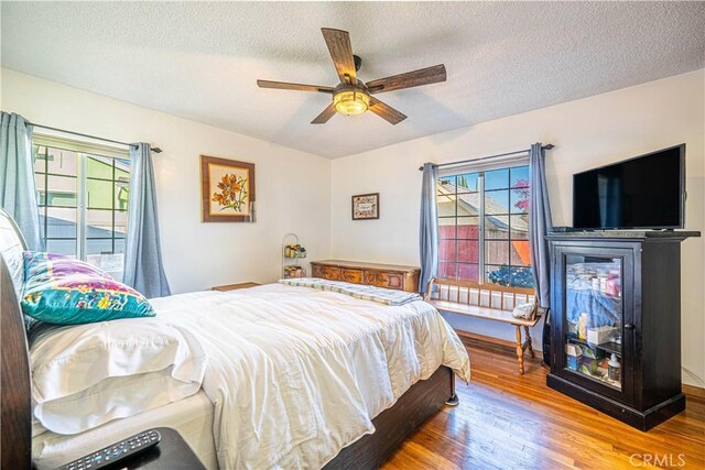 bedroom featuring a multi sided fireplace, a textured ceiling, ceiling fan, and wood finished floors