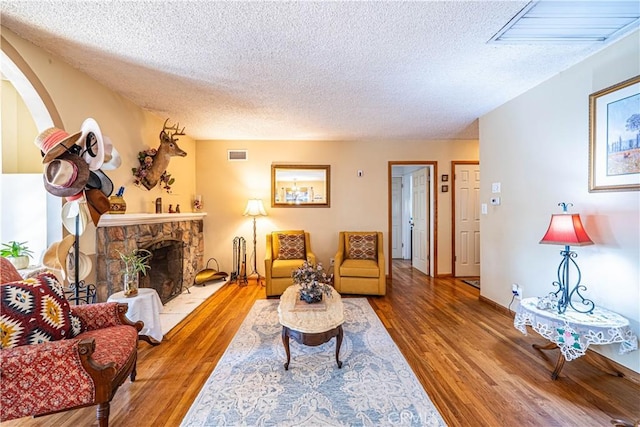 living area with a stone fireplace, wood finished floors, visible vents, and a textured ceiling