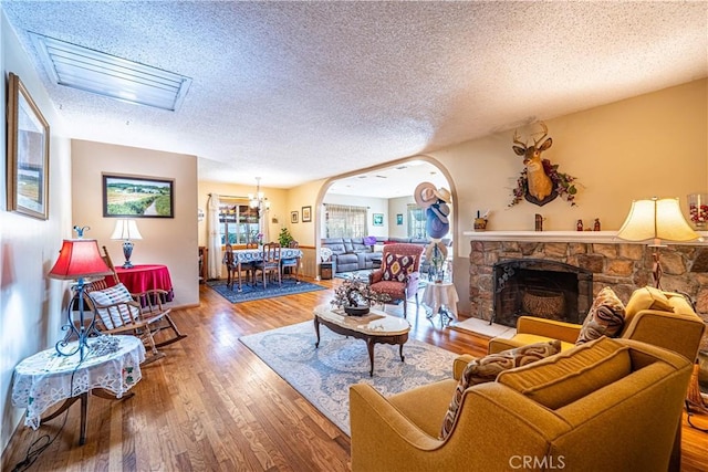 living room with arched walkways, a textured ceiling, wood finished floors, and a fireplace