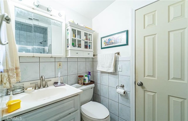 bathroom with vanity, tile walls, toilet, and a shower