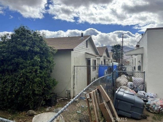 view of home's exterior with stucco siding, a shingled roof, and fence