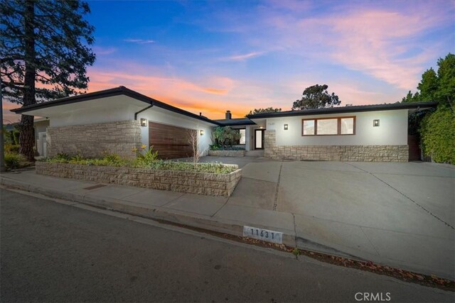 ranch-style home with stone siding, an attached garage, and concrete driveway