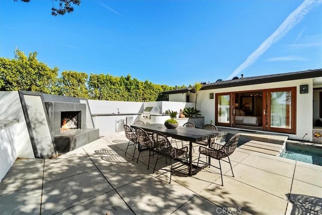 view of patio featuring grilling area, a fenced in pool, a lit fireplace, outdoor dining area, and area for grilling