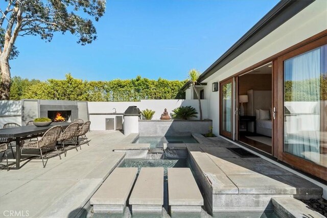 view of patio / terrace with a fenced in pool, exterior kitchen, a lit fireplace, and fence