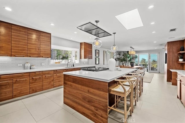 kitchen featuring stovetop, a sink, a kitchen breakfast bar, modern cabinets, and brown cabinets