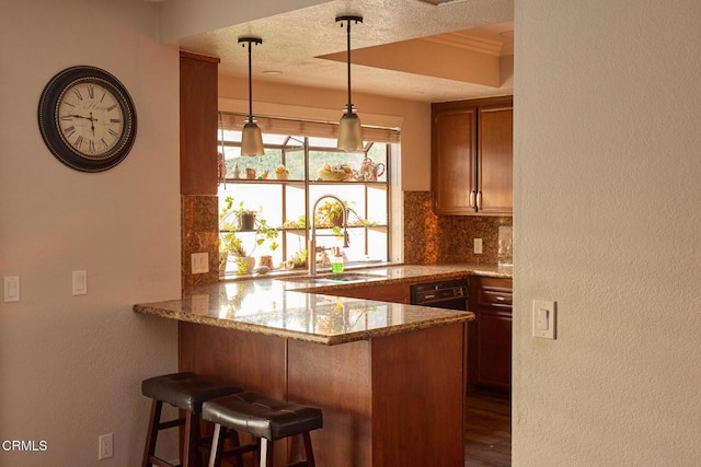 kitchen featuring tasteful backsplash, light stone counters, a peninsula, a textured ceiling, and a sink