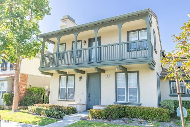 view of front of home featuring stucco siding, a chimney, and a balcony