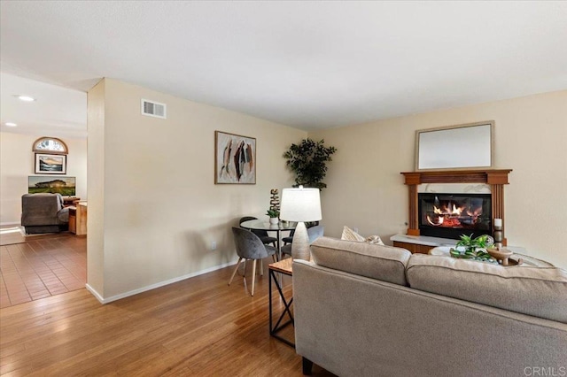 living area with a glass covered fireplace, visible vents, baseboards, and wood finished floors