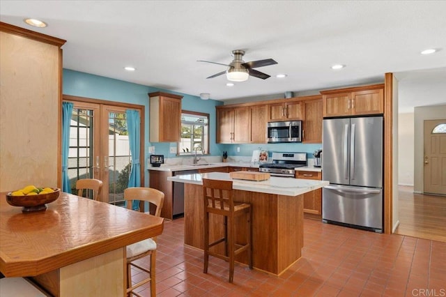 kitchen with a breakfast bar area, a sink, stainless steel appliances, light countertops, and a center island