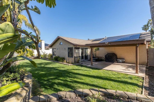 rear view of house featuring stucco siding, a patio, fence, a yard, and solar panels