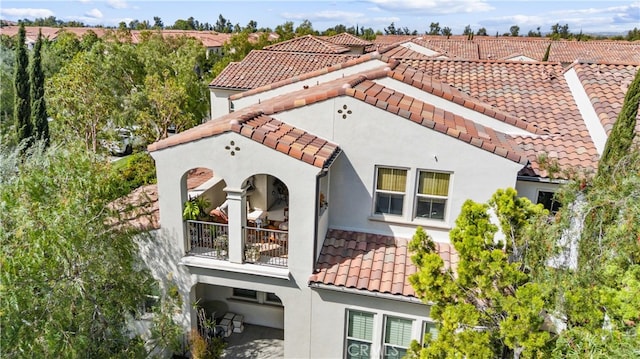 view of side of home with stucco siding, a balcony, and a tile roof