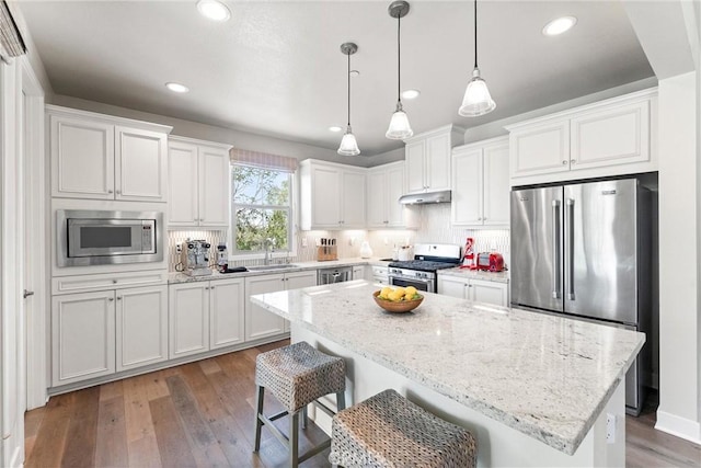 kitchen with a sink, decorative backsplash, wood-type flooring, appliances with stainless steel finishes, and white cabinetry