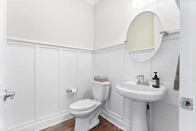 bathroom with a decorative wall, wainscoting, toilet, and wood finished floors