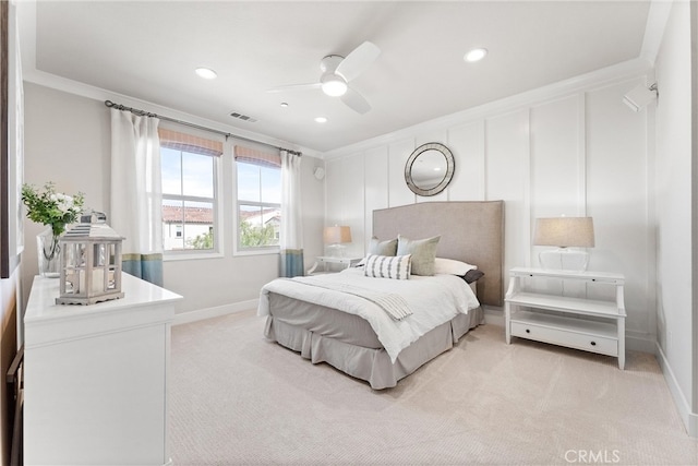 bedroom featuring visible vents, light carpet, ornamental molding, and a decorative wall