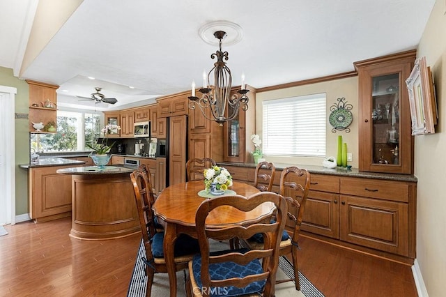 dining room featuring baseboards, ornamental molding, a raised ceiling, ceiling fan with notable chandelier, and light wood-type flooring