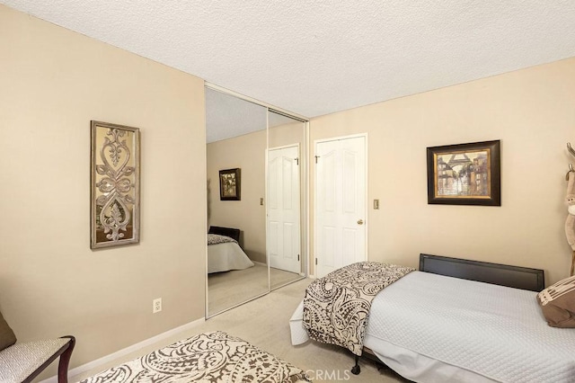 bedroom featuring baseboards, light colored carpet, a closet, and a textured ceiling