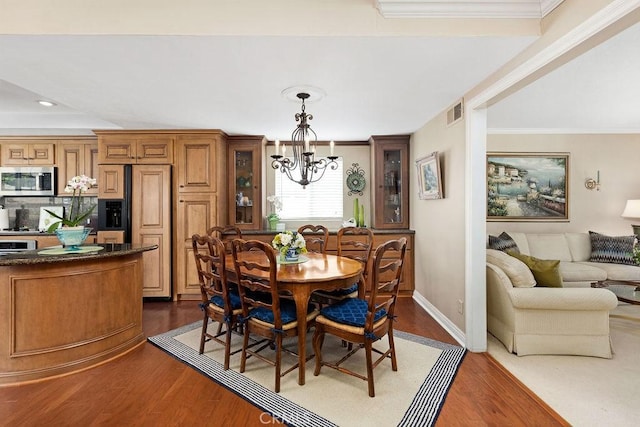 dining space with dark wood finished floors, a notable chandelier, baseboards, and ornamental molding