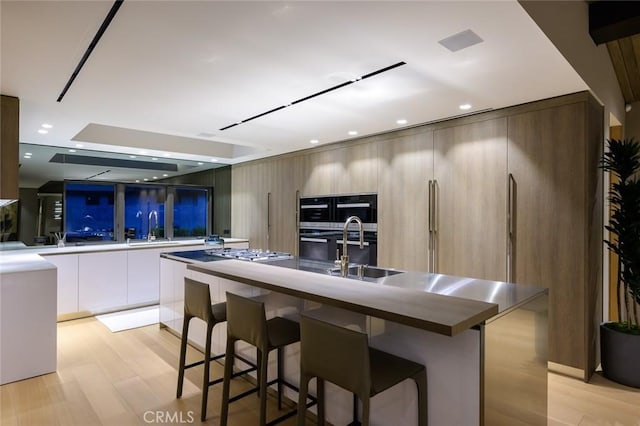 kitchen featuring light wood-type flooring, modern cabinets, a kitchen island with sink, a sink, and a kitchen breakfast bar