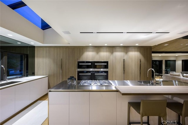 kitchen featuring a sink, a kitchen bar, stainless steel appliances, white cabinetry, and modern cabinets