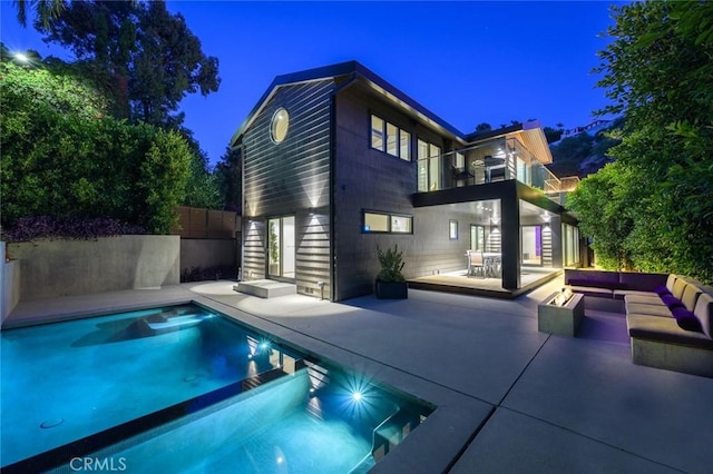 back of house at night featuring an outdoor pool, a patio, a balcony, and fence