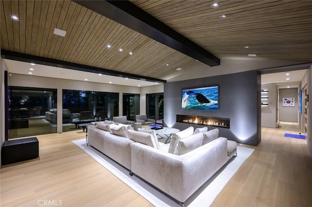 home theater featuring light wood finished floors, a glass covered fireplace, and vaulted ceiling with beams