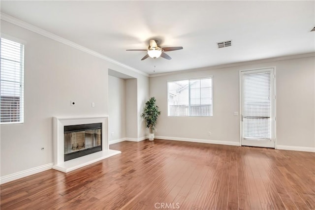 unfurnished living room featuring ornamental molding, a glass covered fireplace, wood finished floors, baseboards, and ceiling fan