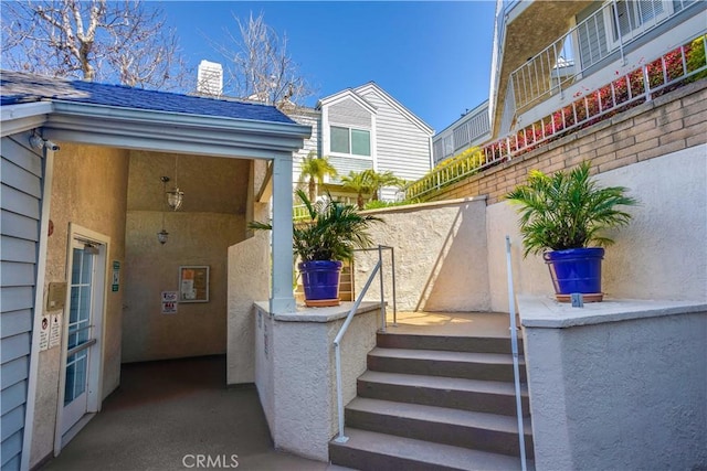 entrance to property featuring a chimney, roof with shingles, and stucco siding