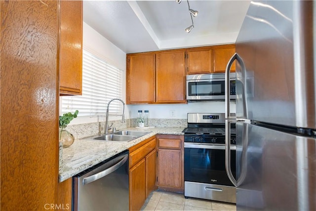 kitchen with light stone counters, light tile patterned flooring, a sink, stainless steel appliances, and brown cabinets