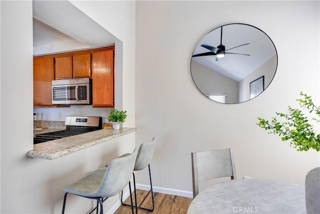 kitchen featuring light countertops, light wood-style floors, appliances with stainless steel finishes, a kitchen bar, and brown cabinets