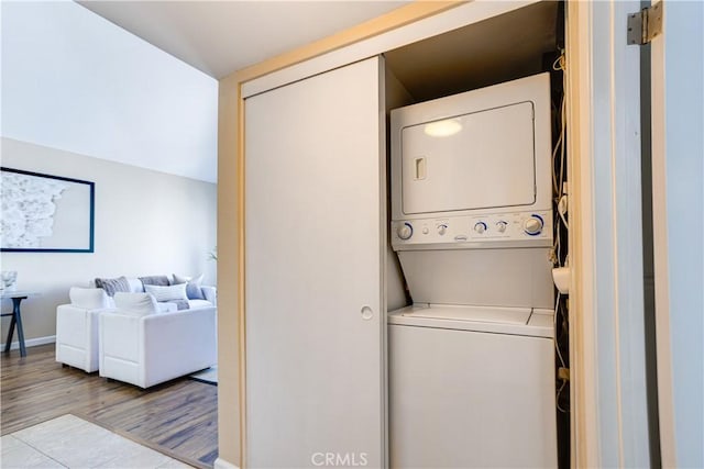 laundry room featuring laundry area, wood finished floors, stacked washer and clothes dryer, and baseboards