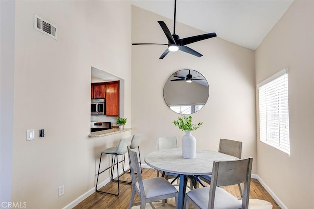 dining area with visible vents, ceiling fan, baseboards, vaulted ceiling, and wood finished floors