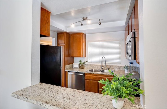 kitchen with track lighting, a tray ceiling, brown cabinets, appliances with stainless steel finishes, and a sink