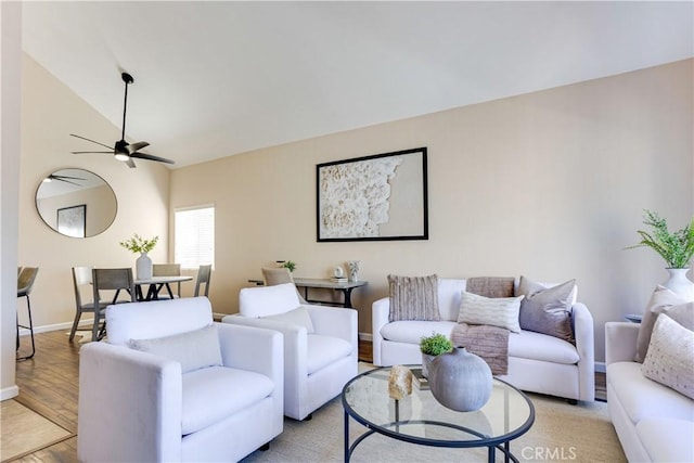 living area featuring ceiling fan, baseboards, light wood-style floors, and vaulted ceiling