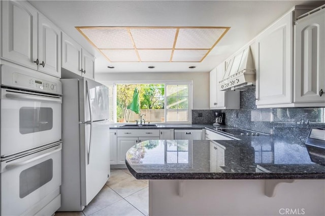 kitchen with white appliances, dark stone counters, a peninsula, a sink, and backsplash