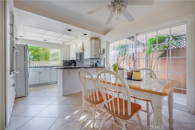 kitchen featuring a peninsula, freestanding refrigerator, a sink, wall chimney range hood, and backsplash