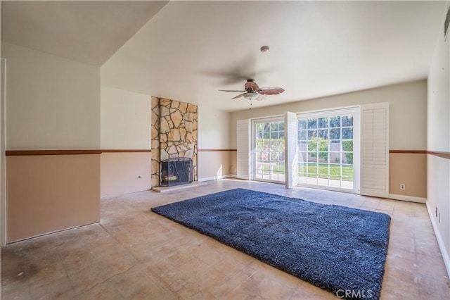 unfurnished living room with a stone fireplace, baseboards, and a ceiling fan