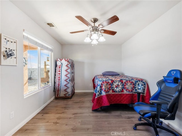 bedroom with a ceiling fan, wood finished floors, visible vents, and baseboards