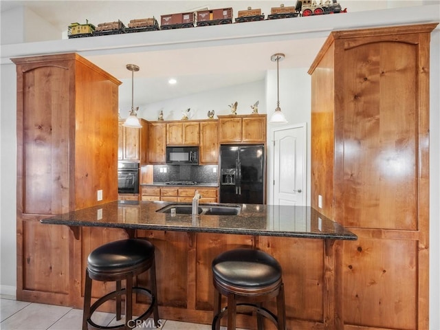 kitchen featuring black appliances, a sink, dark stone countertops, brown cabinetry, and decorative backsplash